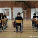 boys and girls sit with their backs to the camera in an exam hall at separated desk.