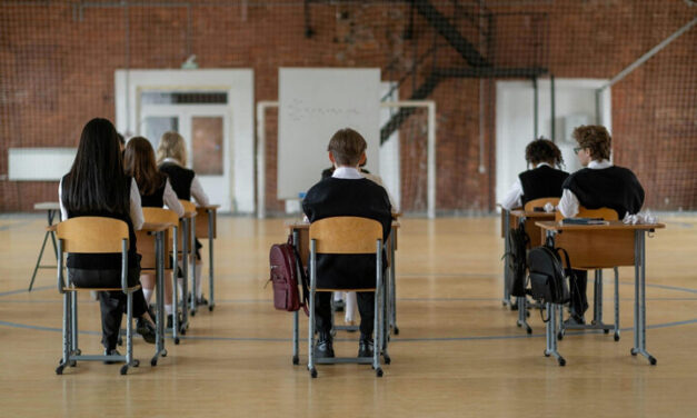boys and girls sit with their backs to the camera in an exam hall at separated desk.