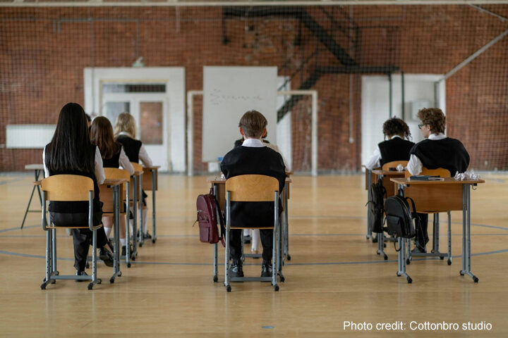 boys and girls sit with their backs to the camera in an exam hall at separated desk.
