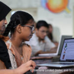 Technology-driven STEM learning in action. Three students sit around a laptop in a classroom.