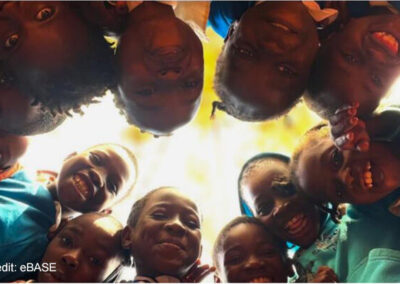 Children stand in a circle and look down to the camera in the middle of the floor.