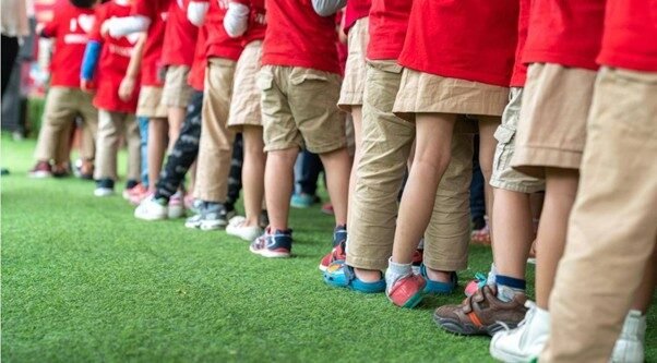 Image of legs of children in a line, they are all wearing red tops