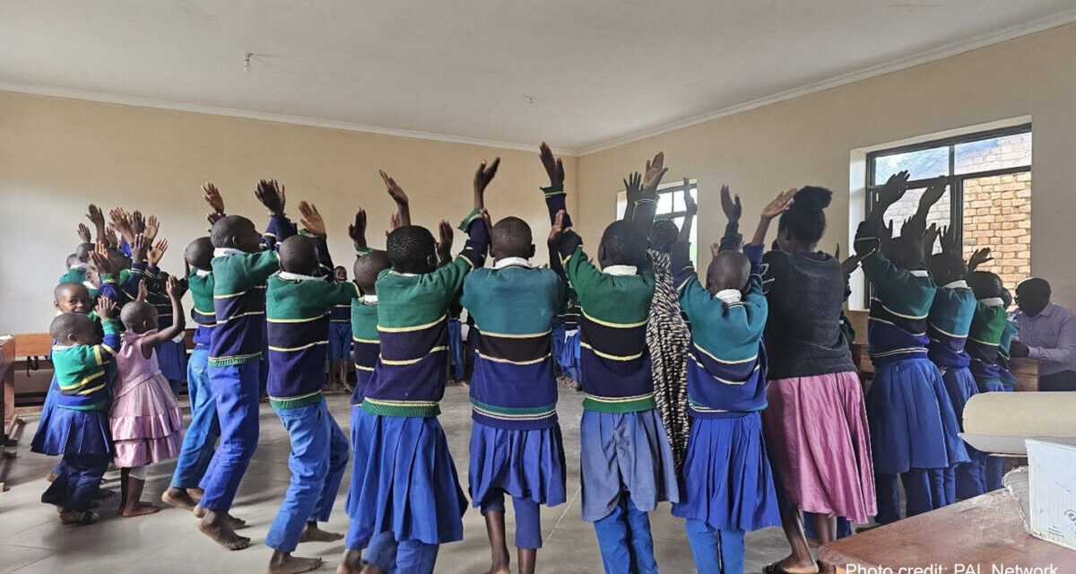 Children take part in a learning activity jumping in a circle with hands above their heads, around the classroom, Tanzania.