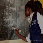 Teacher writes on the blackboard in Kasonga Primary School, Kyangwali Refugee Settlement, Uganda
