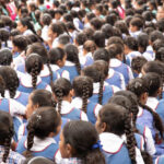 Schoolgirls in uniforms sit with their back to the camera, India.