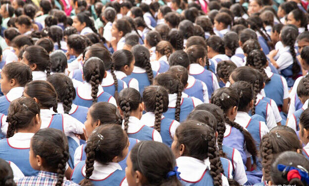 Schoolgirls in uniforms sit with their back to the camera, India.