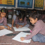 A trio of students sit on the floor working together in a classroom in India.