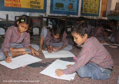 A trio of students sit on the floor working together in a classroom in India.