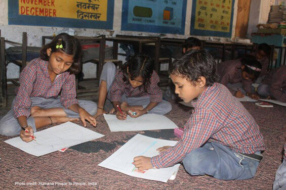 A trio of students sit on the floor working together in a classroom in India.