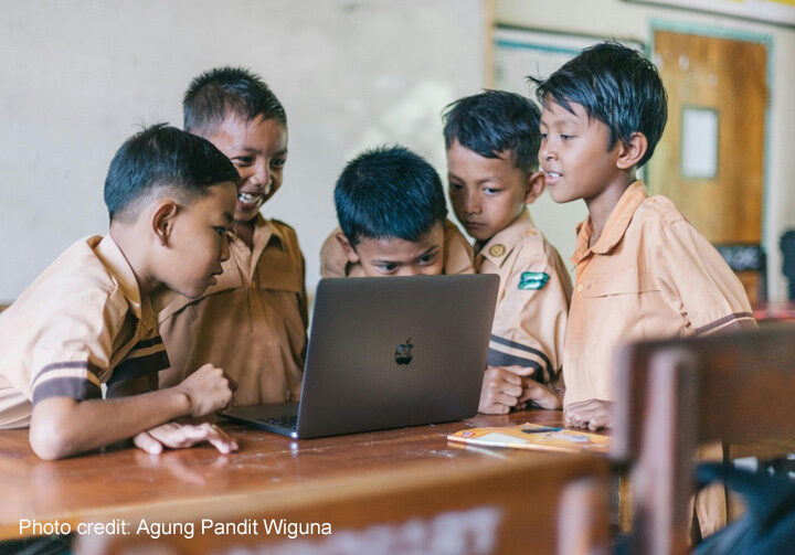 Boys crowd around a laptop, Indonesia.
