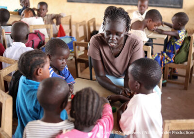 Nyuriel, a learning support assistant is teaching a group of children sitting around a table in a classroom in Kakuma refugee camp in Kenya.