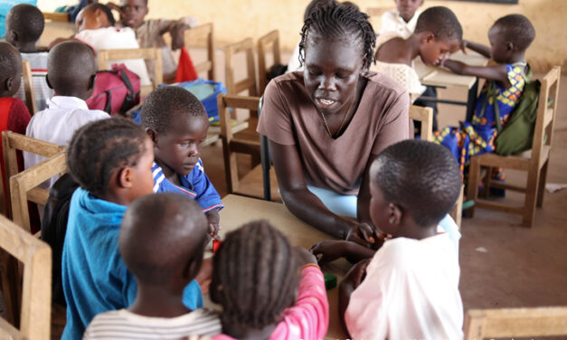 Nyuriel, a learning support assistant is teaching a group of children sitting around a table in a classroom in Kakuma refugee camp in Kenya.