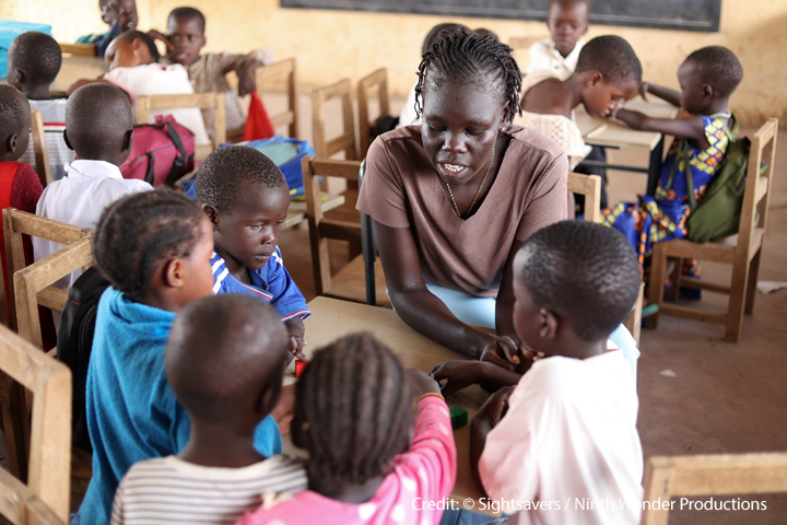 Nyuriel, a learning support assistant is teaching a group of children sitting around a table in a classroom in Kakuma refugee camp in Kenya.