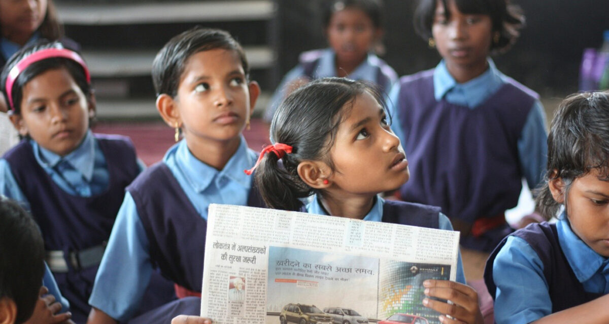 A schoolgirl sits in a government classroom holding a newspaper, Chhattisgarh, India