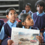 A schoolgirl sits in a government classroom holding a newspaper, Chhattisgarh, India