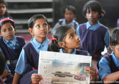 A schoolgirl sits in a government classroom holding a newspaper, Chhattisgarh, India