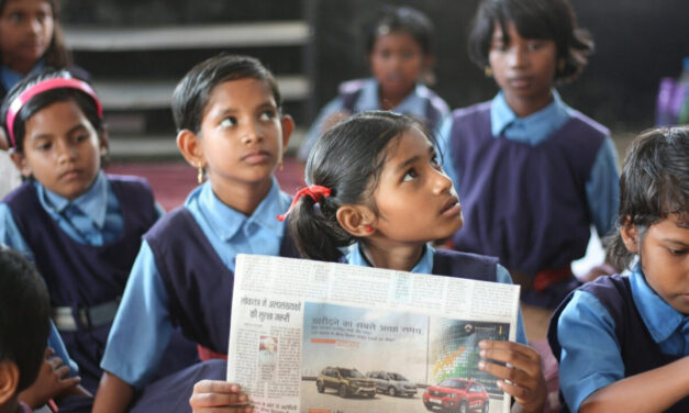 A schoolgirl sits in a government classroom holding a newspaper, Chhattisgarh, India