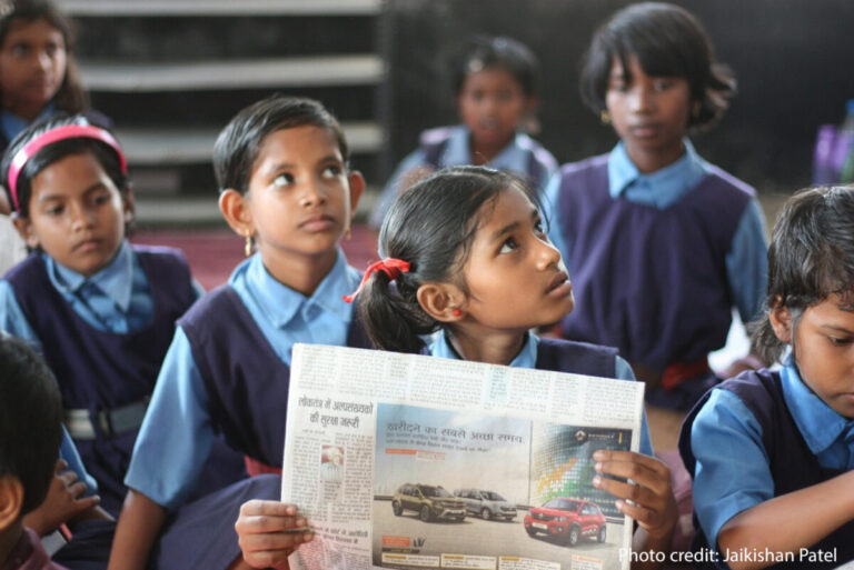A schoolgirl sits in a government classroom holding a newspaper, Chhattisgarh, India