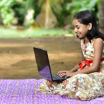 Girl sits on a blanket with a laptop, India.