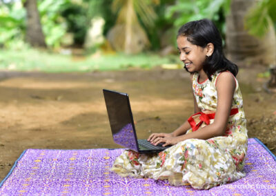 Girl sits on a blanket with a laptop, India.