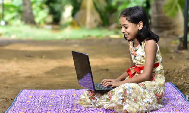 Girl sits on a blanket with a laptop, India.