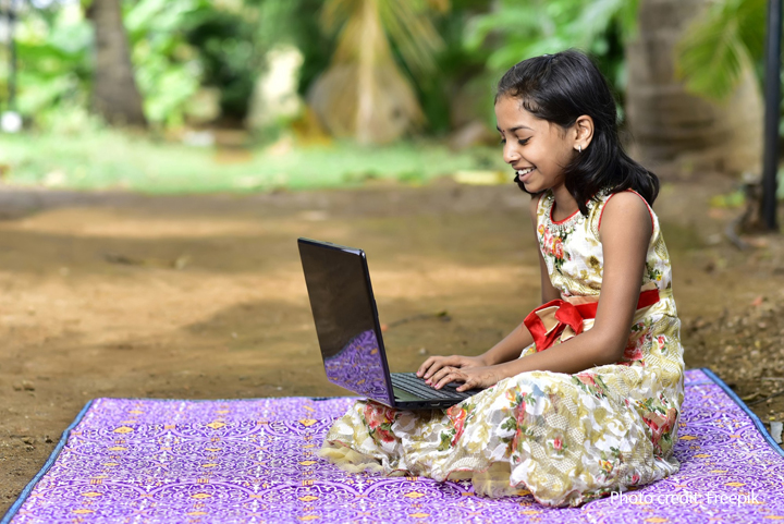 Girl sits on a blanket with a laptop, India.