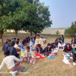 Children sit outside doing an interactive class.