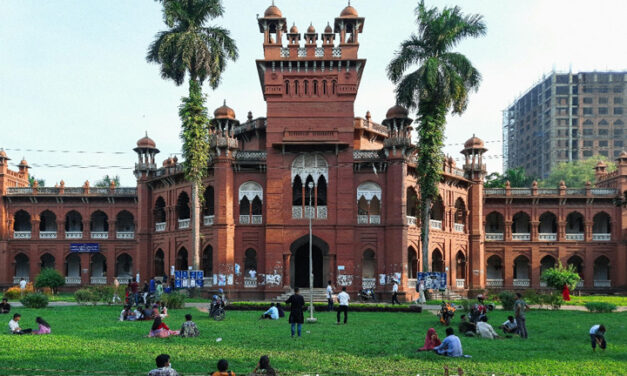 Students sit outside on the grass on a university campus.