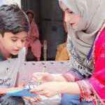 A female teacher sits with a young boy helping him with reading.