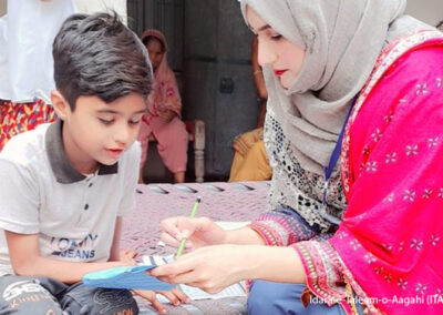 A female teacher sits with a young boy helping him with reading.