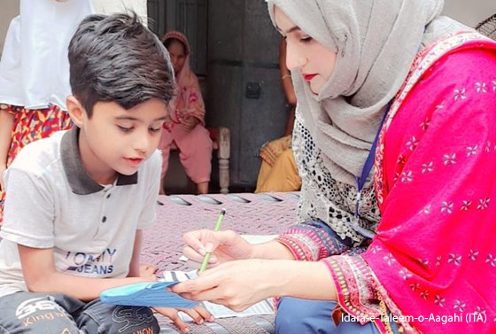 Beyond Enrolment 1 A female teacher sits with a young boy helping him with reading.