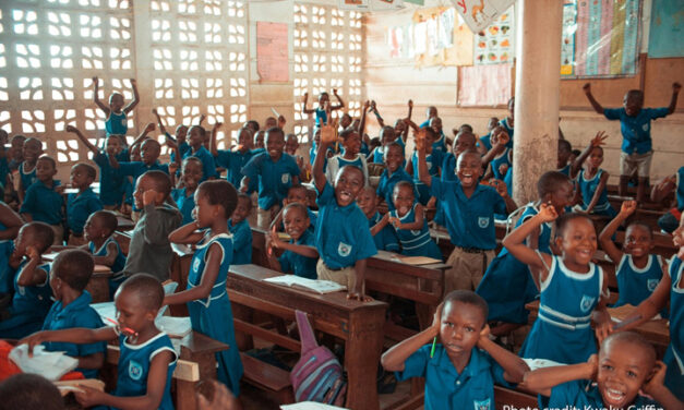 A group of schoolchildren energetically participating in a classroom activity indoors.