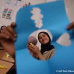 A girl, Hayat, smiles through a cut-out paper shape during a psychosocial activity at a non-formal education centre in Latakia, Syria.