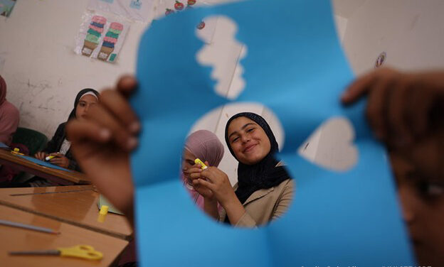 A girl, Hayat, smiles through a cut-out paper shape during a psychosocial activity at a non-formal education centre in Latakia, Syria.