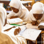 Girls sit looking at textbooks in a classroom in Nigeria.