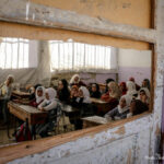 Children sit in a destroyed classroom, Syria. Viewed through an broken window