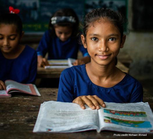 Girl sits in her classroom with an open textbook, Bangladesh